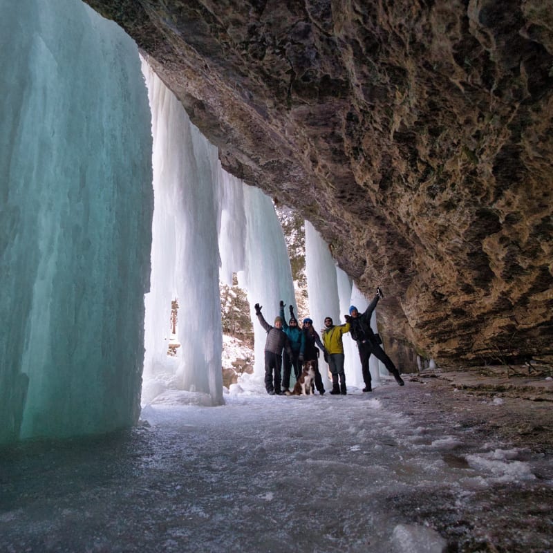 Group of hikers under a frozen waterfall.