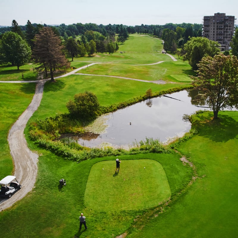 Vue aérienne d'un terrain de golf avec plan d'eau, sentier et voiturette.